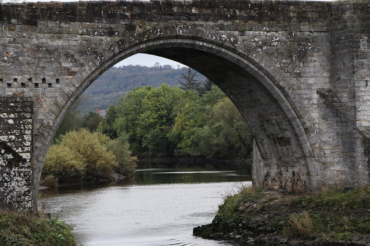 Pasarela de piedra en arco sobre río, símbolo de infraestructuras cuyo